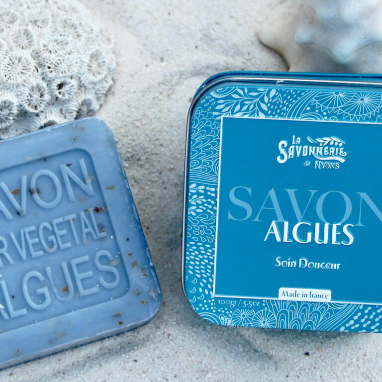 Savon aux algues de 100 g et sa boîte en métal illustrée, posés sur le sable, La Savonnerie de Nyons