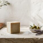 Cube de savon traditionnel a l'huile d'olive pose sur une pierre, avec sel marin, olives et lavande - illustration, La Savonnerie de Nyons