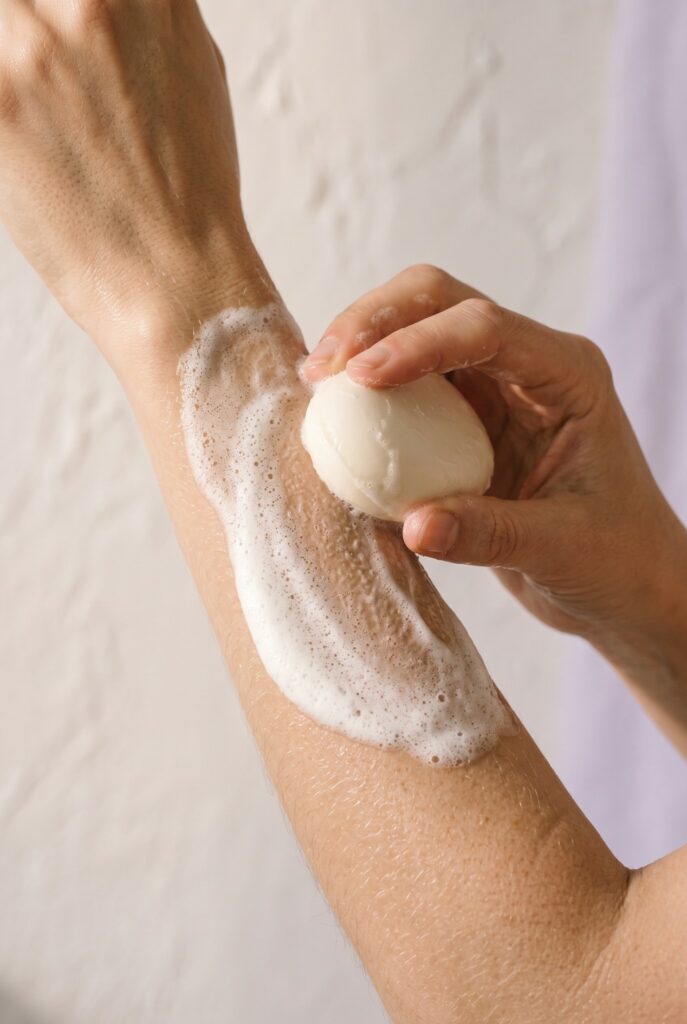 Main qui fait mousser un savon rond sur la peau d'un avant-bras, mousse blanche compacte et onctueuse, La Savonnerie de Nyons