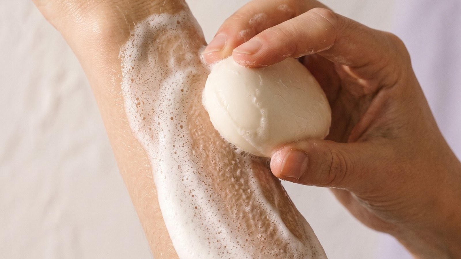 Main qui fait mousser un savon rond sur la peau d'un avant-bras, mousse blanche onctueuse - La Savonnerie de Nyons